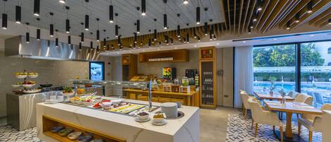 A modern hotel breakfast area with a central island, buffet, seating area, and large windows.