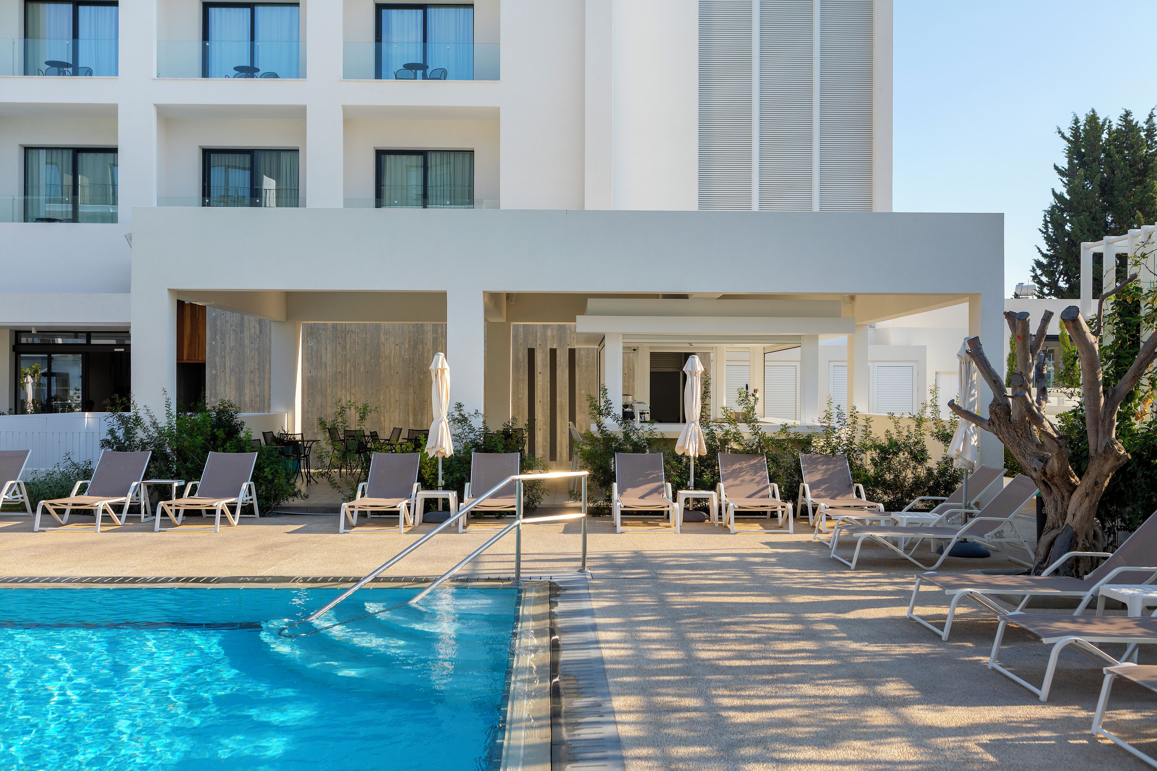 A poolside area with lounge chairs and umbrellas, a clear pool, and a modern building with balconies.
