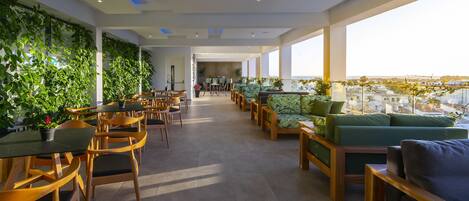 A modern lounge area with wooden furniture, green cushions, and a view of the city.