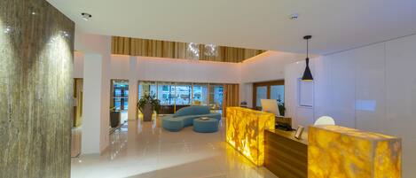 A modern lobby with a marble reception desk, a blue sofa, and a large plant.