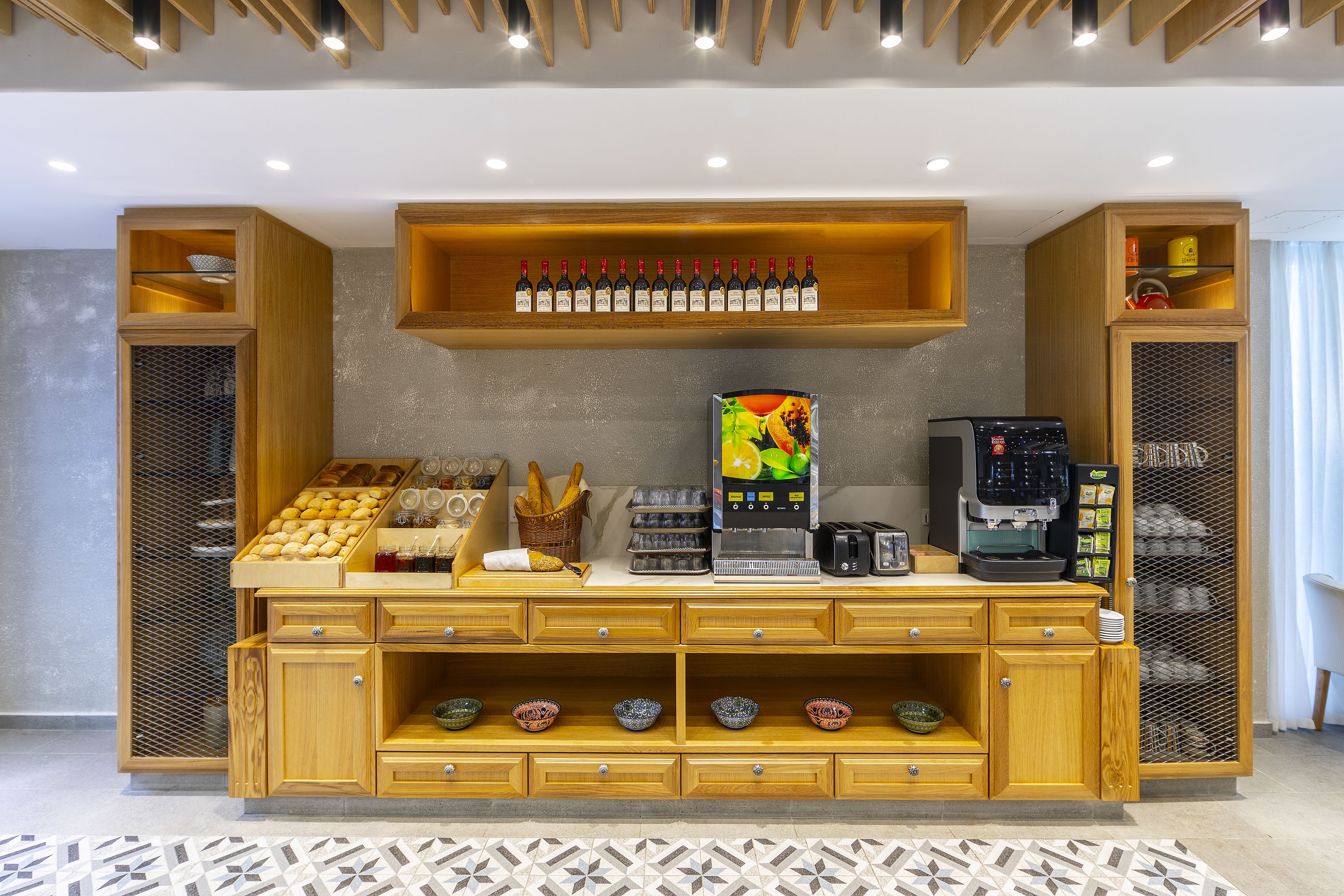 Habitación de hotel con un mostrador buffet de madera, una máquina de café y una selección de botellas de vino.