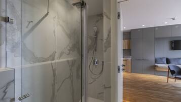 Un baño moderno con ducha de vidrio, paredes de mármol y suelo de madera.