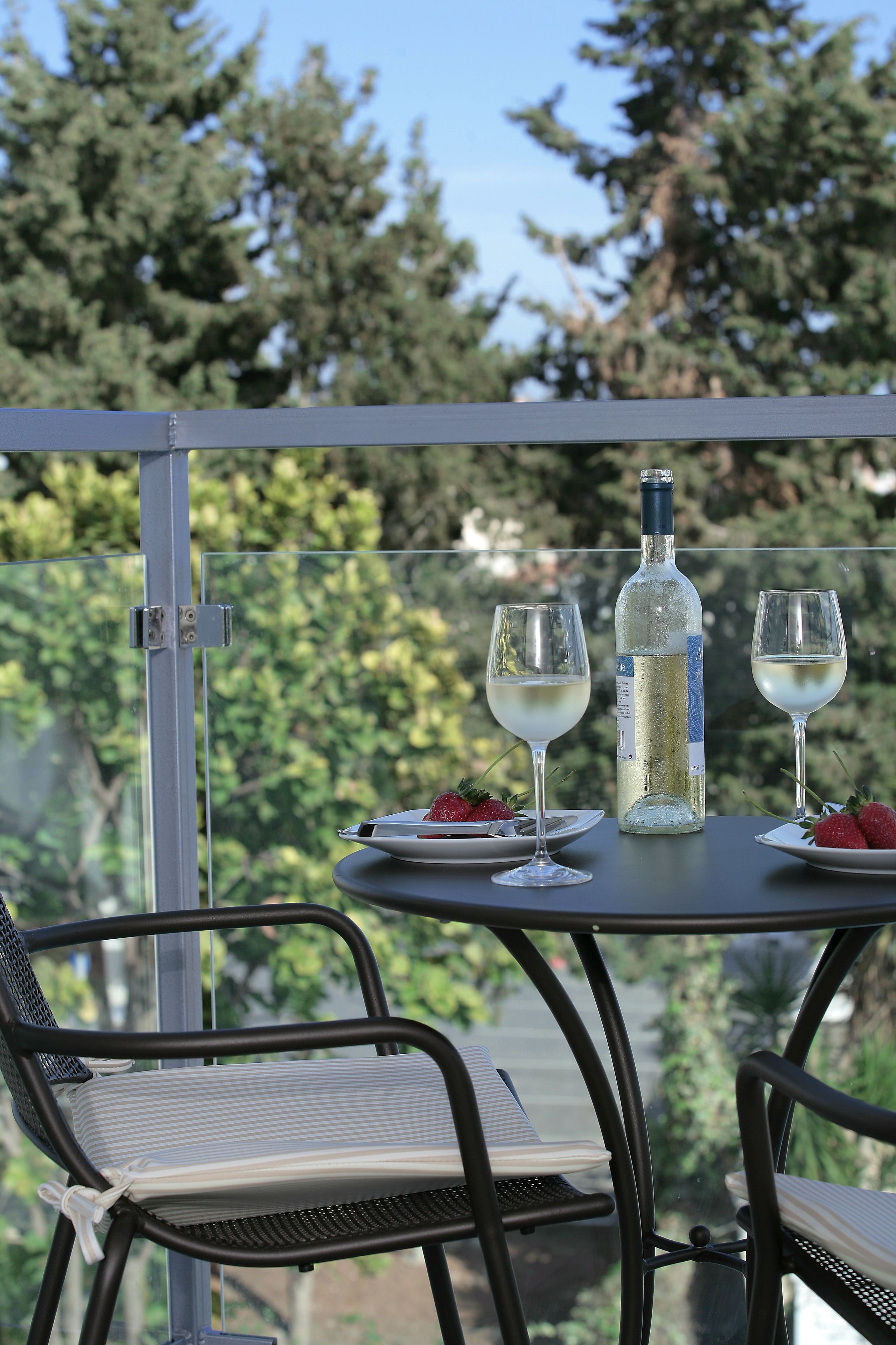 Ein Balkon mit Tisch für zwei Personen, ausgestattet mit einer Flasche, Gläsern und einem Stuhl mit Kissen.
