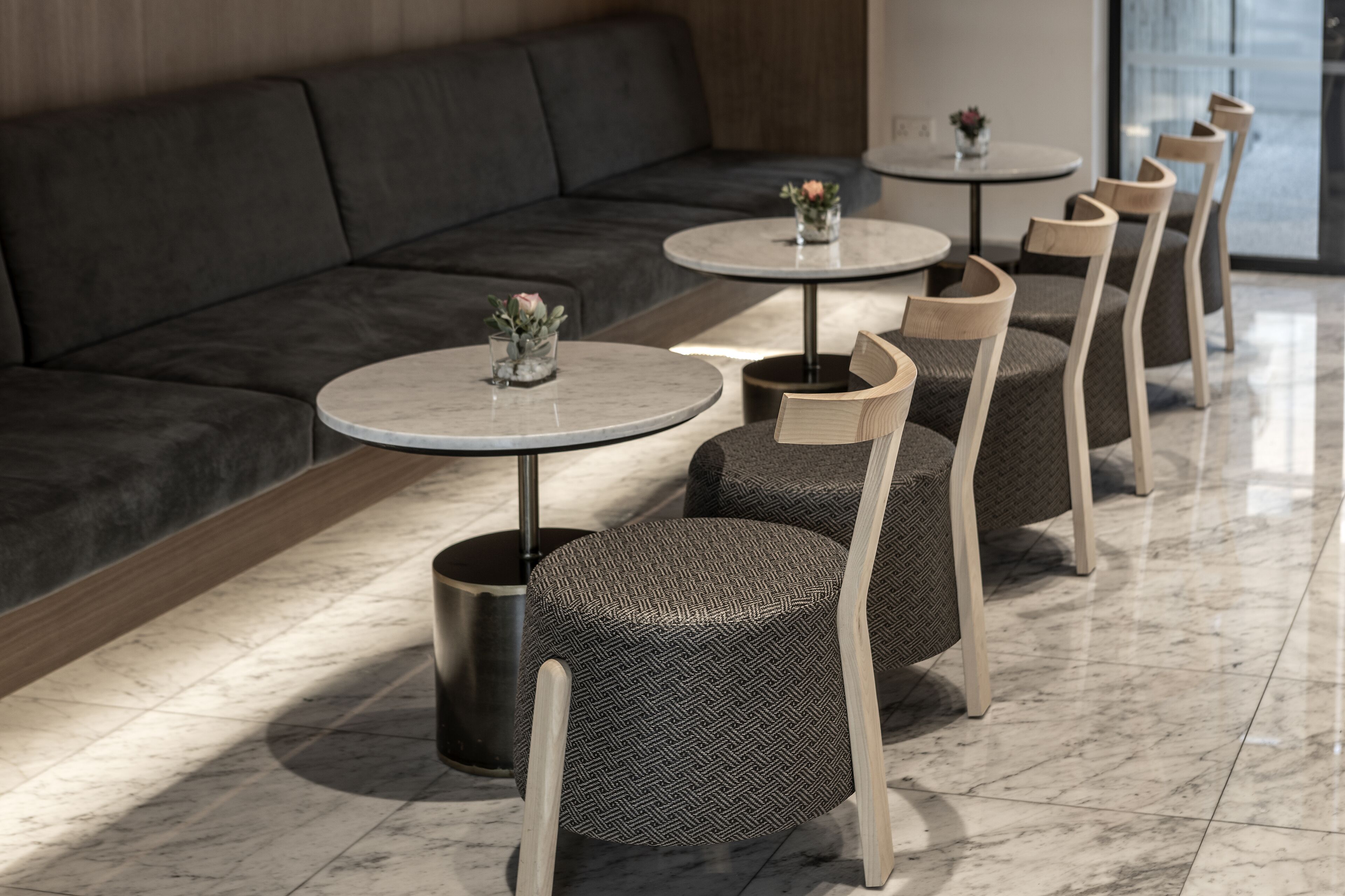 A modern lounge area with a dark sofa, round tables with chairs, and small potted plants.