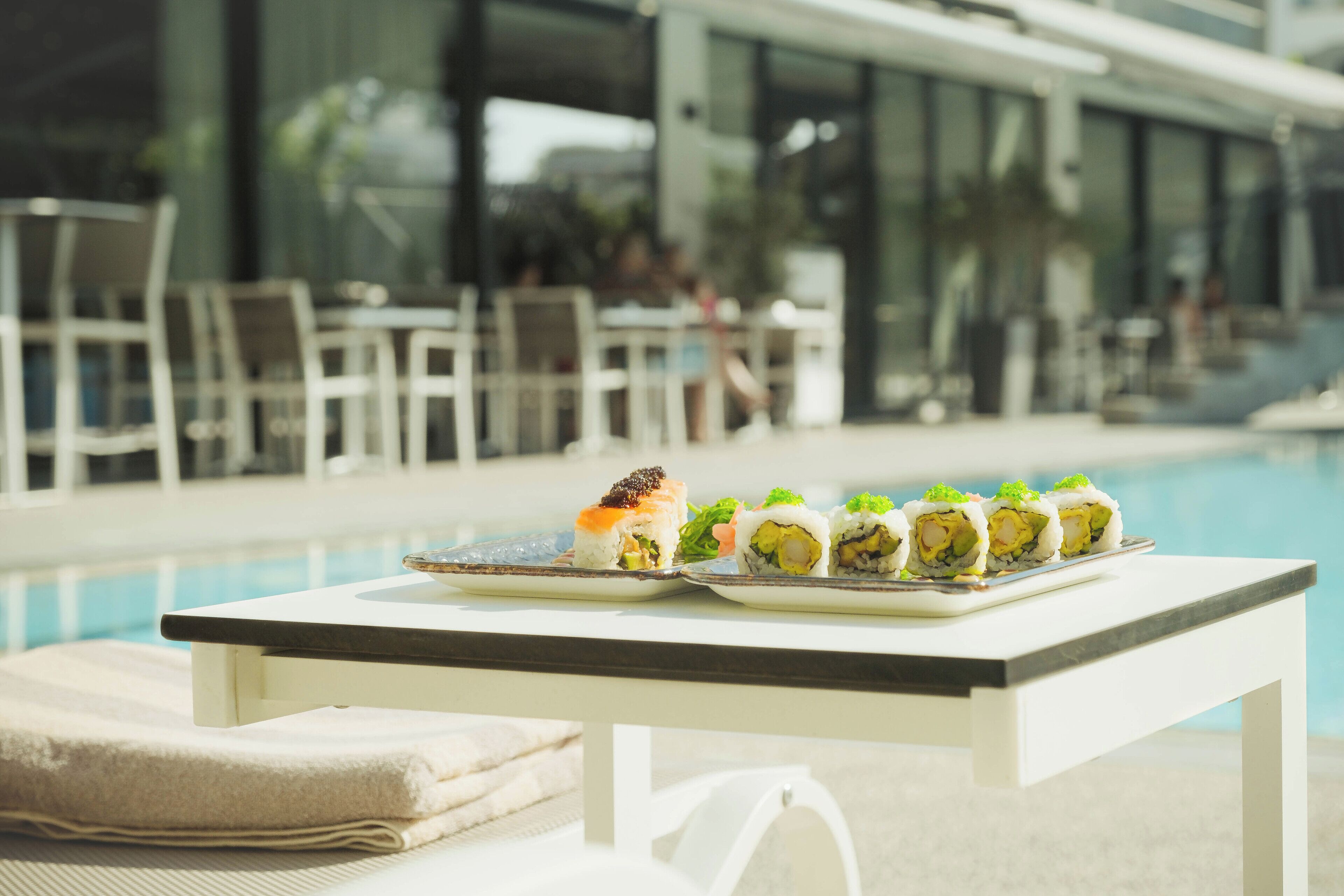 Een tafel bij het zwembad met een schaal sushi en een handdoek op een ligbed.