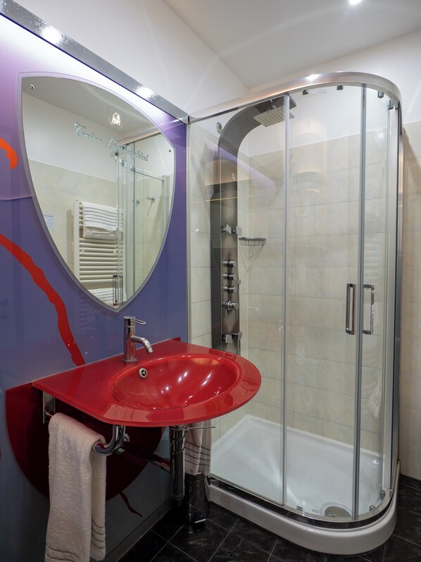 A bathroom with a red sink, a glass shower enclosure, and a large mirror.