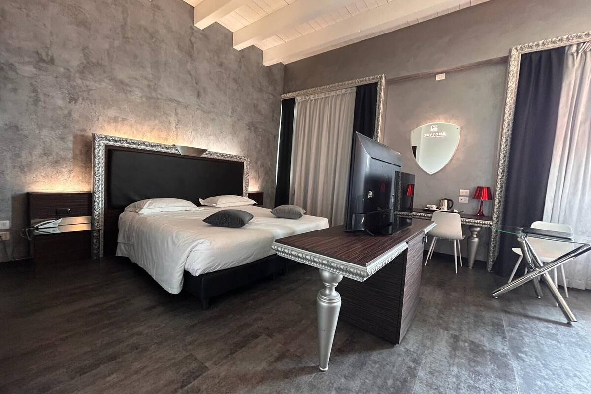 A modern hotel room with a large bed, a desk, a TV, and a mirror.