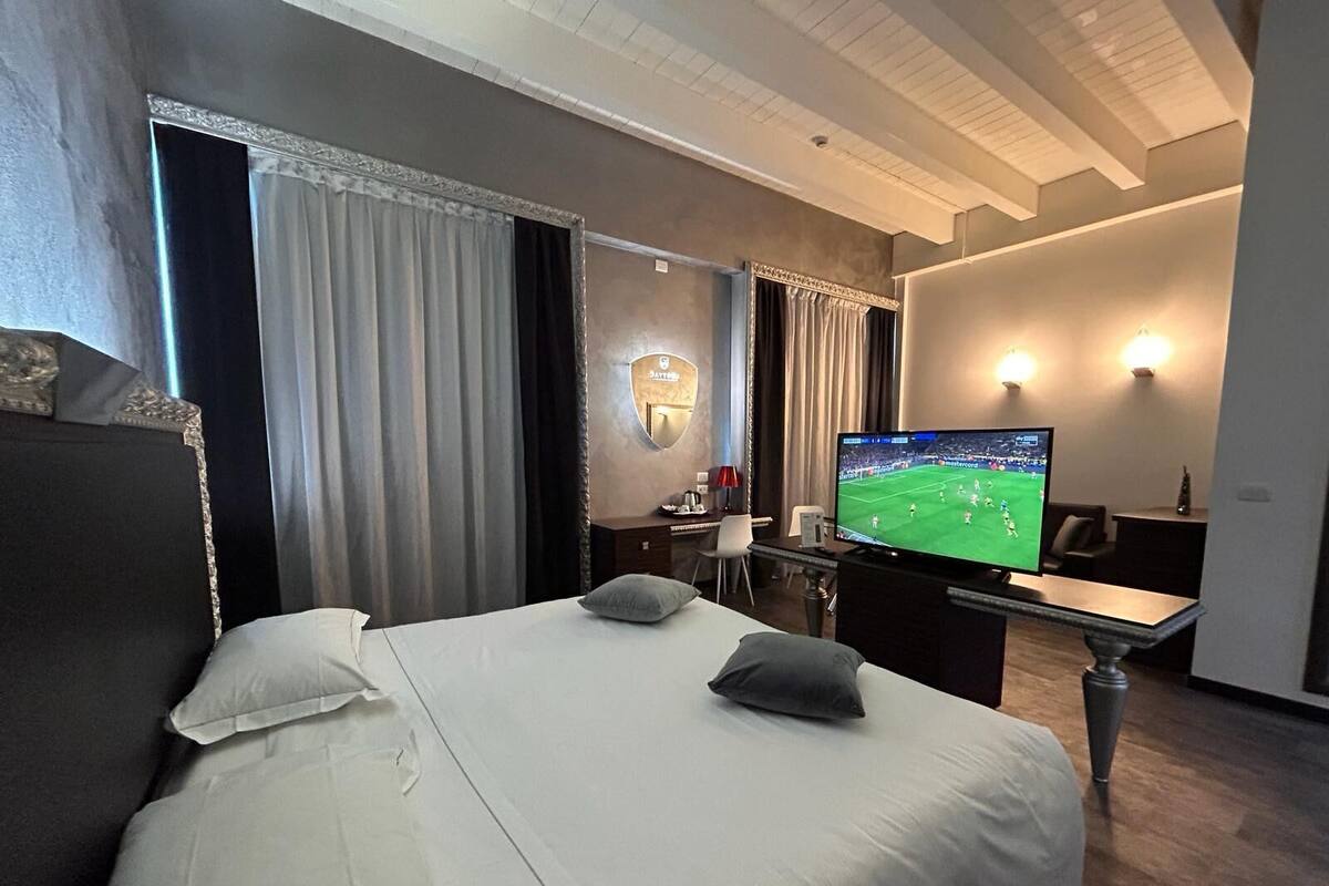 A hotel room with a large bed, a desk, a television, and a mirror.