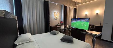 A hotel room with a large bed, a desk, a television, and a mirror.
