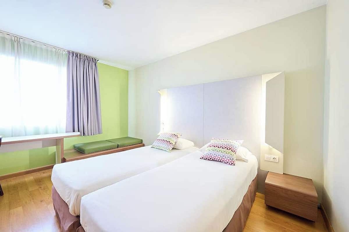 Una habitación de hotel con dos camas, un escritorio y un banco.