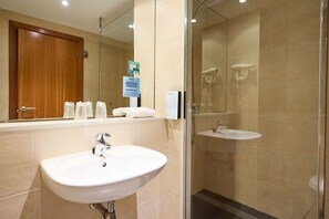 Ein Hotelbad mit Waschbecken, Spiegel und Duschkabine aus Glas.