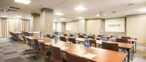 A conference room with multiple tables and chairs, water bottles, and a projector screen displaying "Campanile Hotel Restaurant".