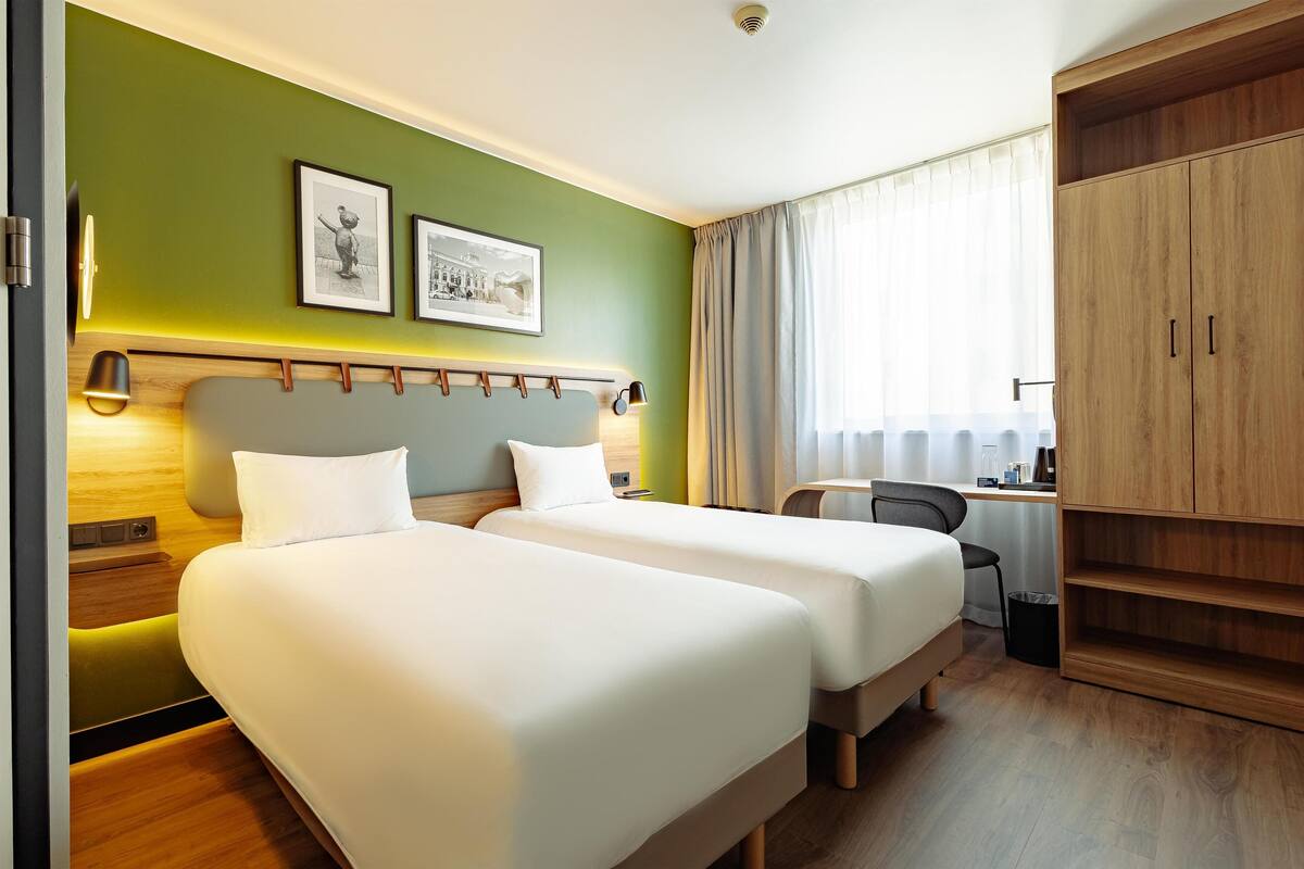 Ein Hotelzimmer mit zwei Betten, einem Schreibtisch, einem Stuhl und einem Kleiderschrank.