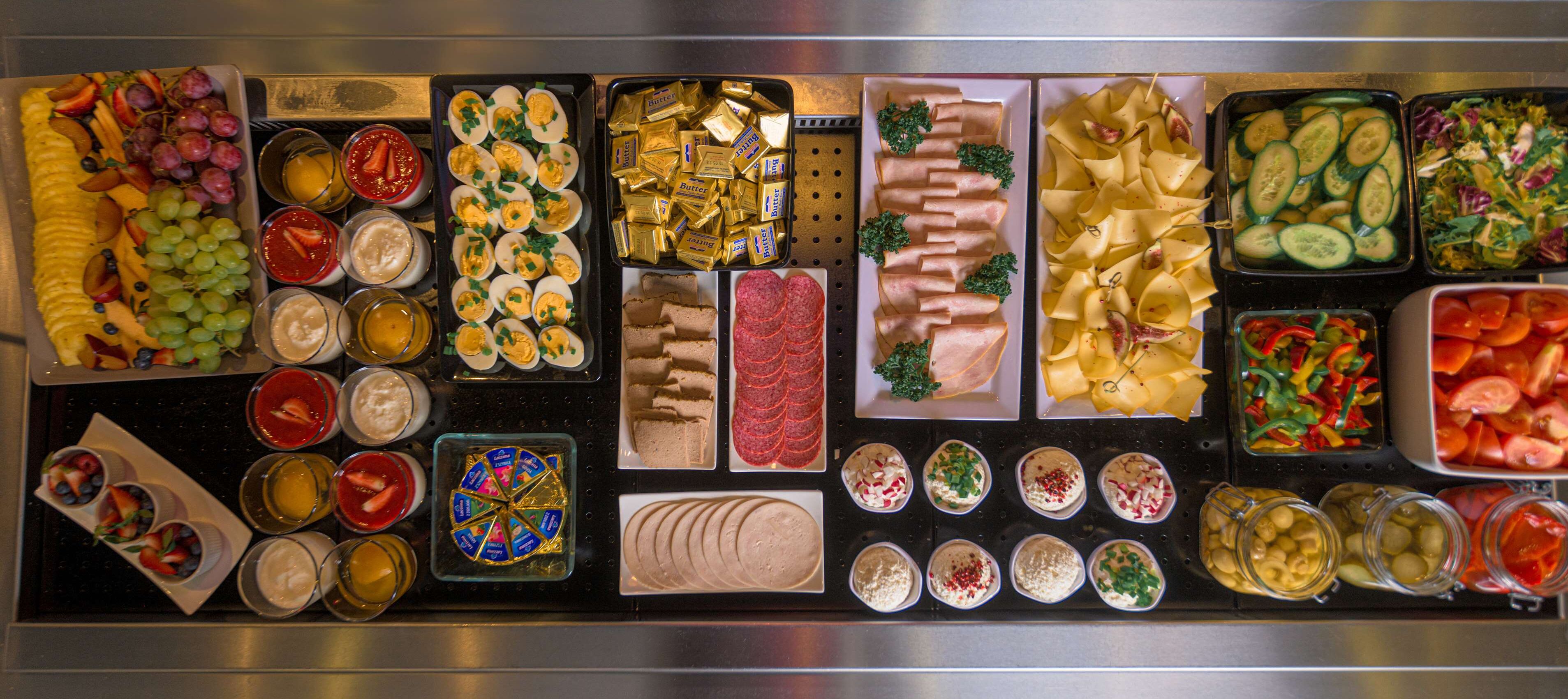 Buffet com diversos alimentos, incluindo frutas, queijos, carnes e saladas.