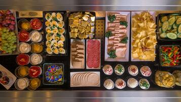 Buffet com diversos alimentos, incluindo frutas, queijos, carnes e saladas.