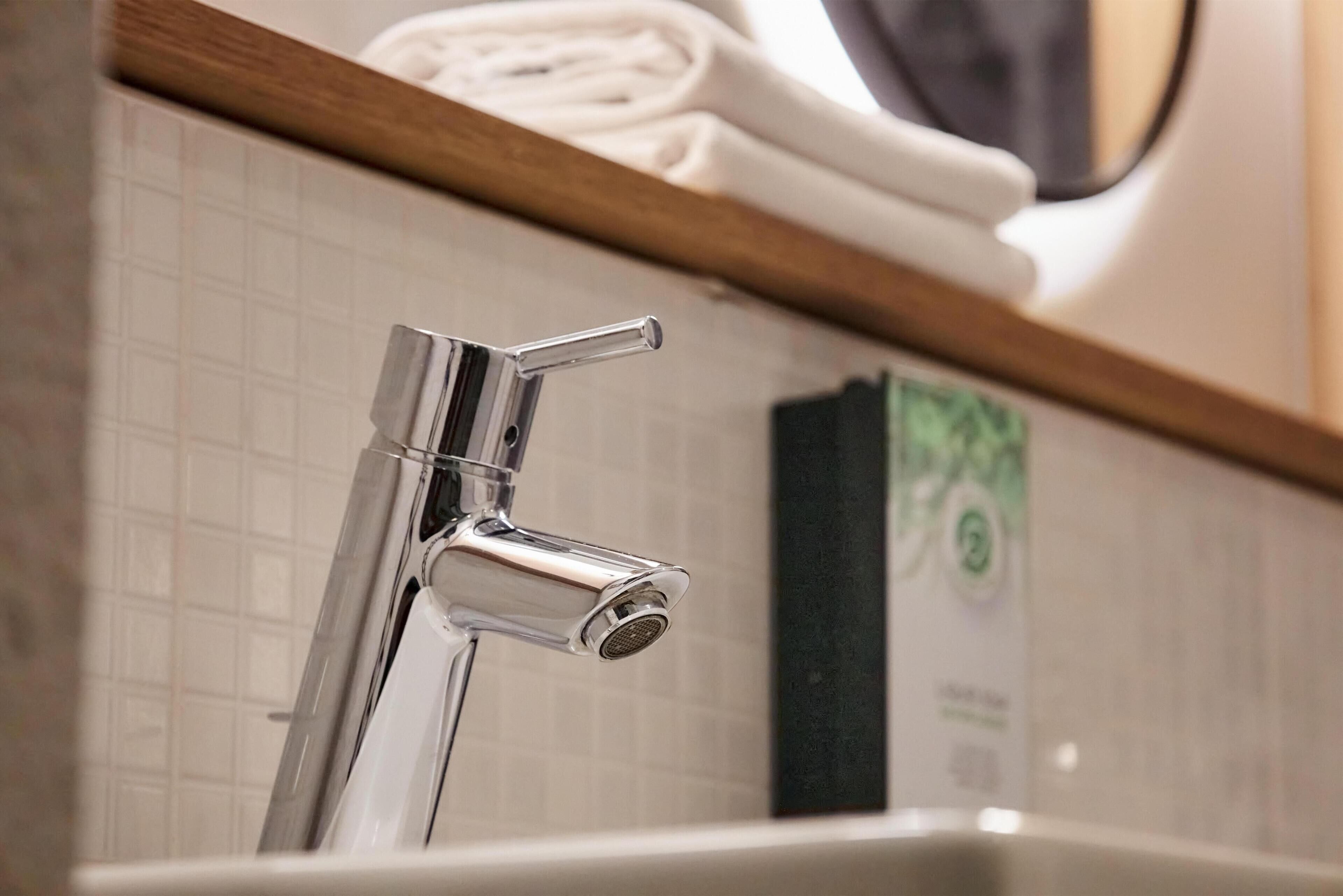 Un baño con grifo cromado, lavamanos blanco y toallero con toallas dobladas.