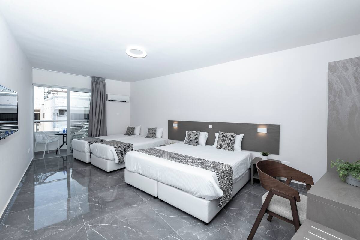 A modern hotel room with two beds, a seating area, and a view of the city.