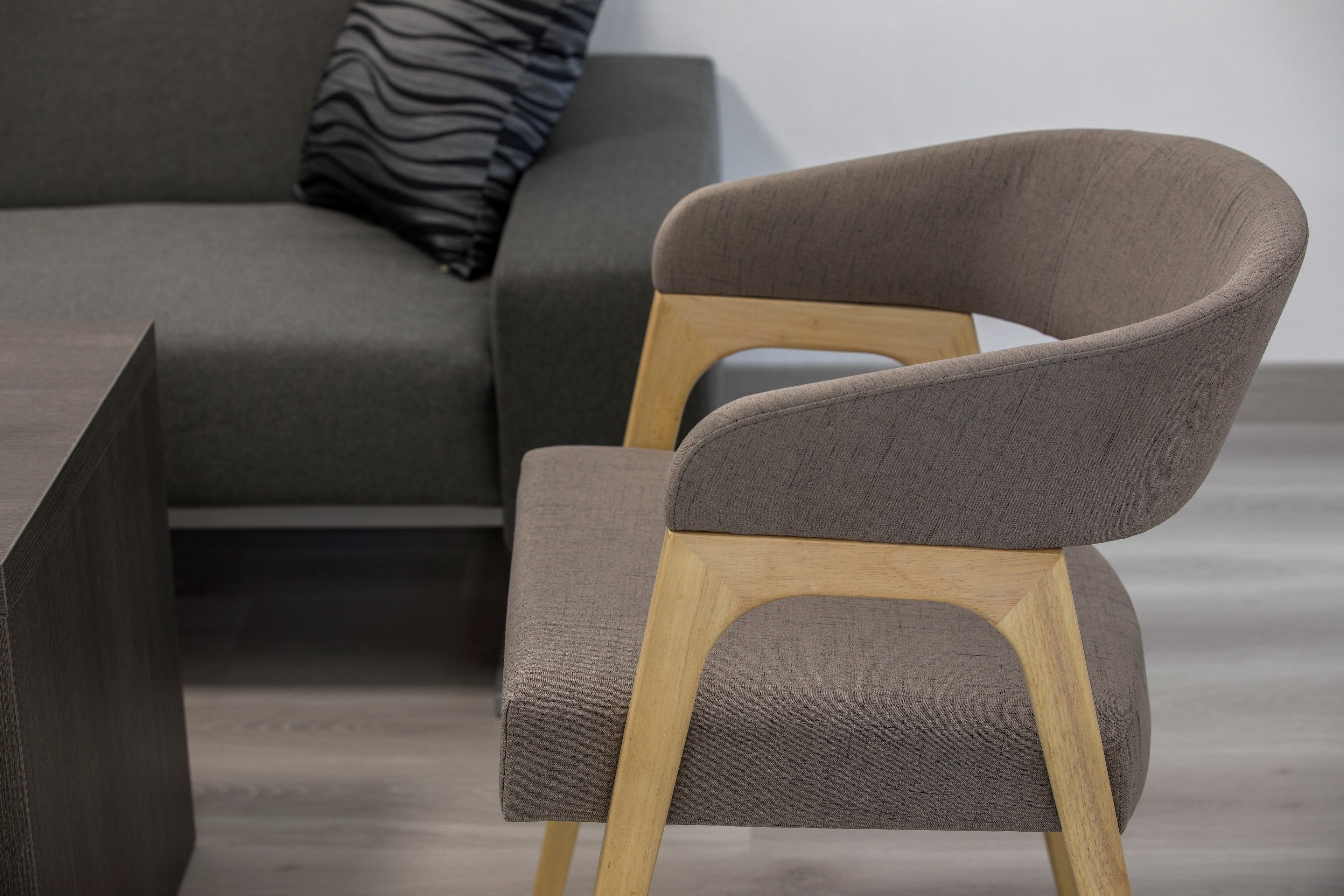 Een moderne fauteuil met houten frame en grijze bekleding, geplaatst in een minimalistische woonkamer.