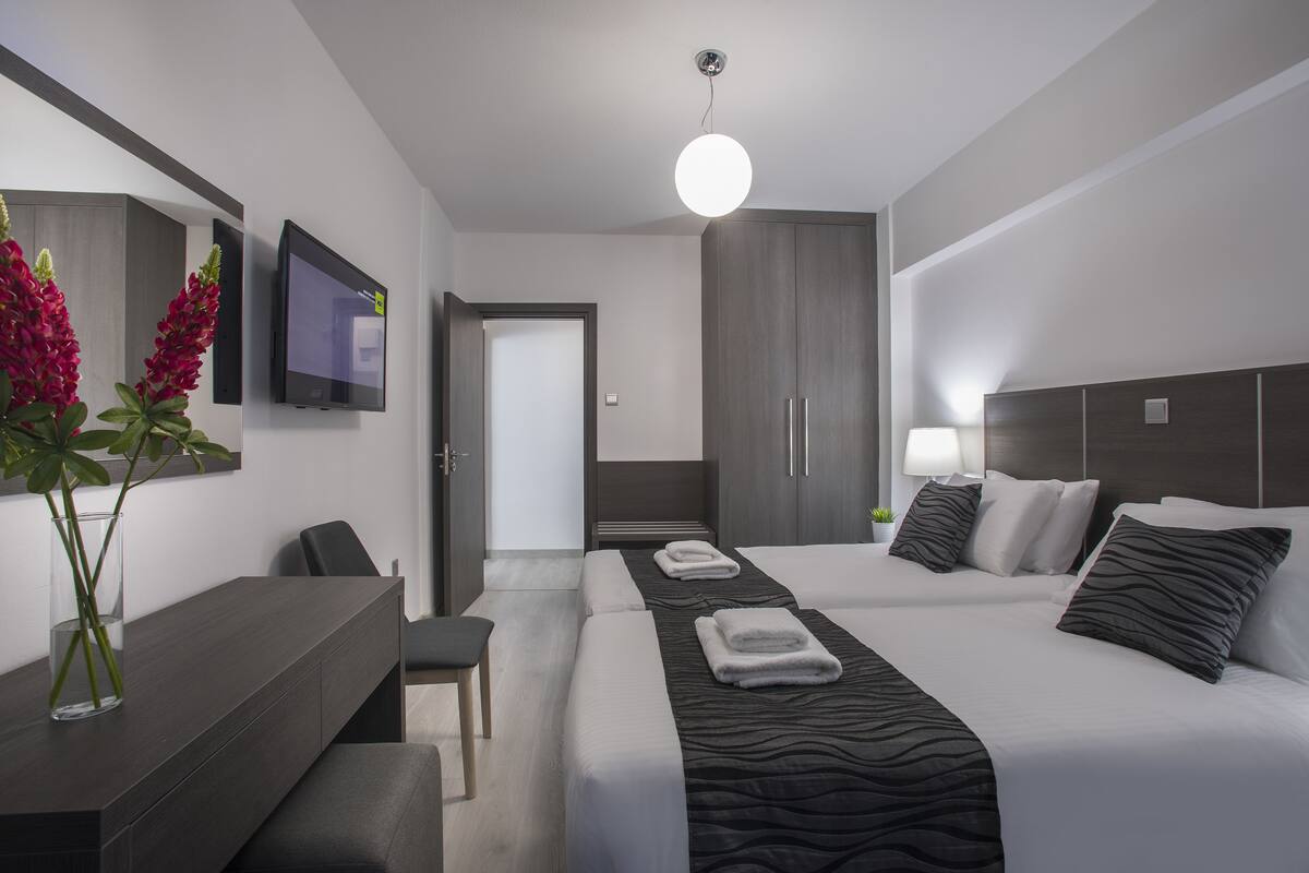 A modern hotel room with a large bed, a desk, a chair, a TV, and a wardrobe.