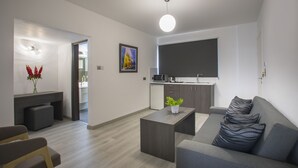A modern living room with a grey sofa, a coffee table, a dining area with a kitchen in the background, and a flat-screen TV mounted on the wall. - Blazer Residence (Larnaca)