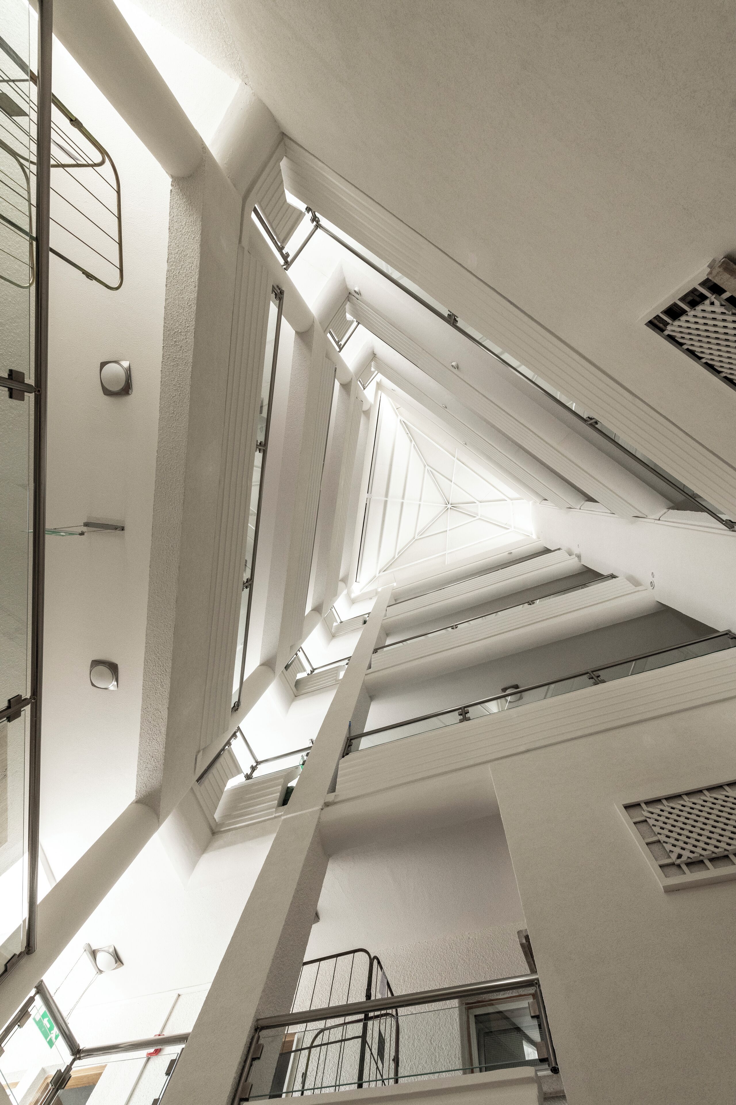 A high-ceilinged interior with a central skylight, white walls, and a staircase leading to upper levels.