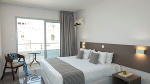 A hotel room with a bed, a chair, a small table, and a view of the outside. - Blazer Residence (Larnaca)