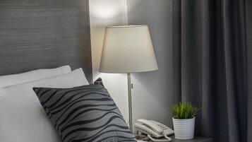 A hotel room with a bed, a zebra-patterned pillow, a lamp, a phone, and a potted plant.