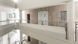 A multi-level interior with a glass railing, a door with an emergency exit sign, and a wall-mounted intercom. - Blazer Residence (Larnaca)