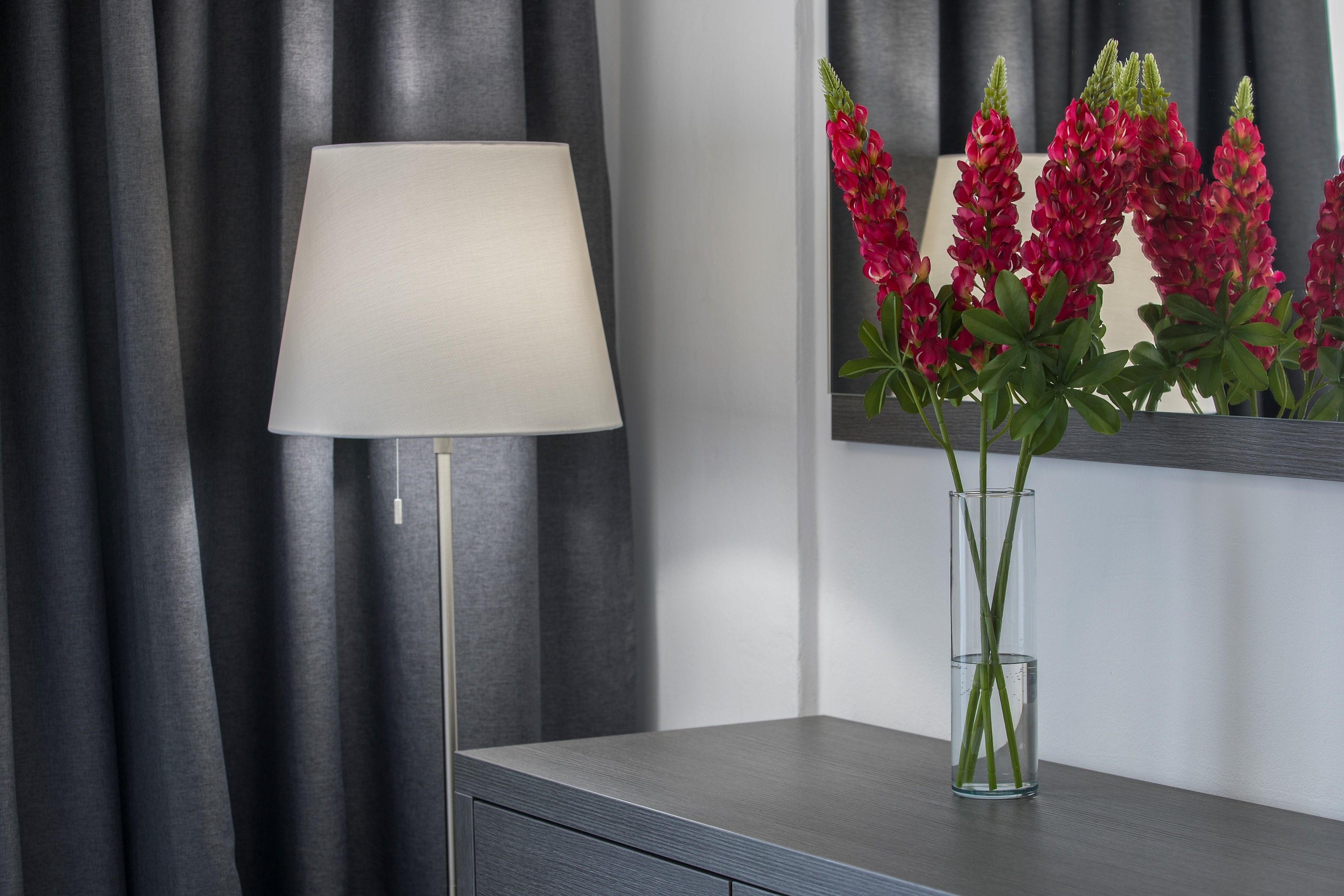 A modern room with a grey sofa, a floor lamp, and a vase with red flowers.