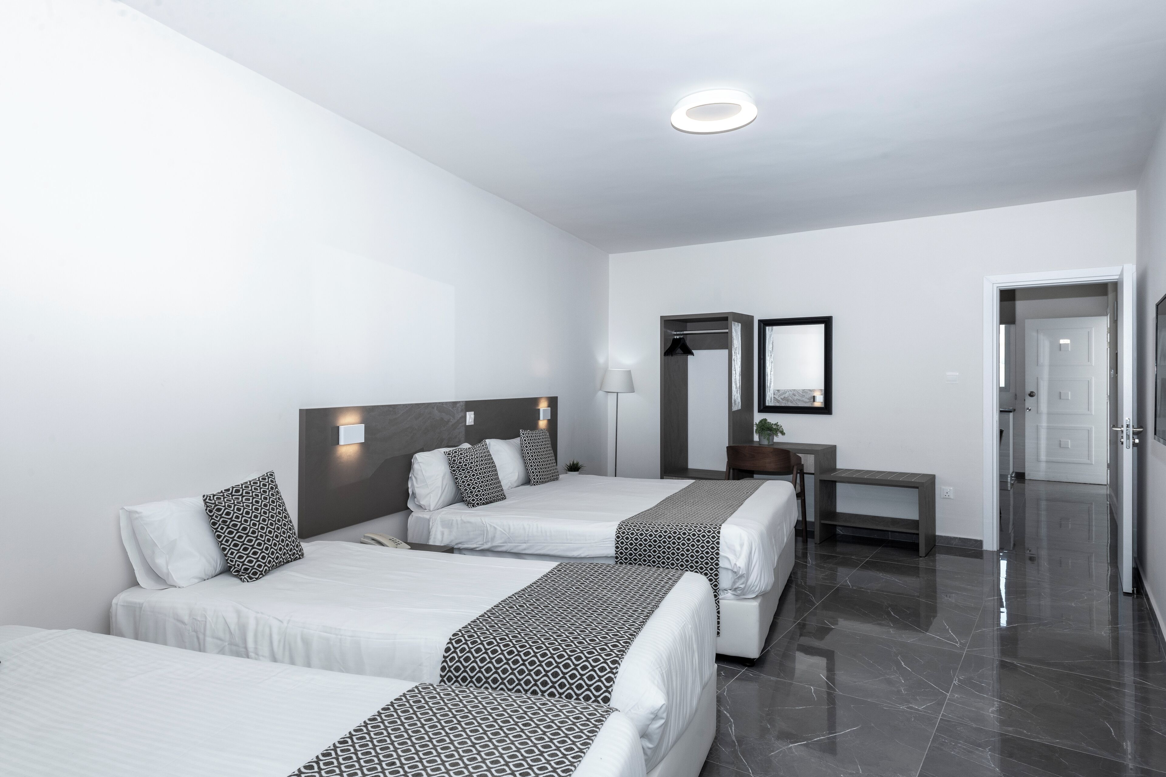 Une chambre d’hôtel avec deux lits, un bureau, un miroir et une porte.