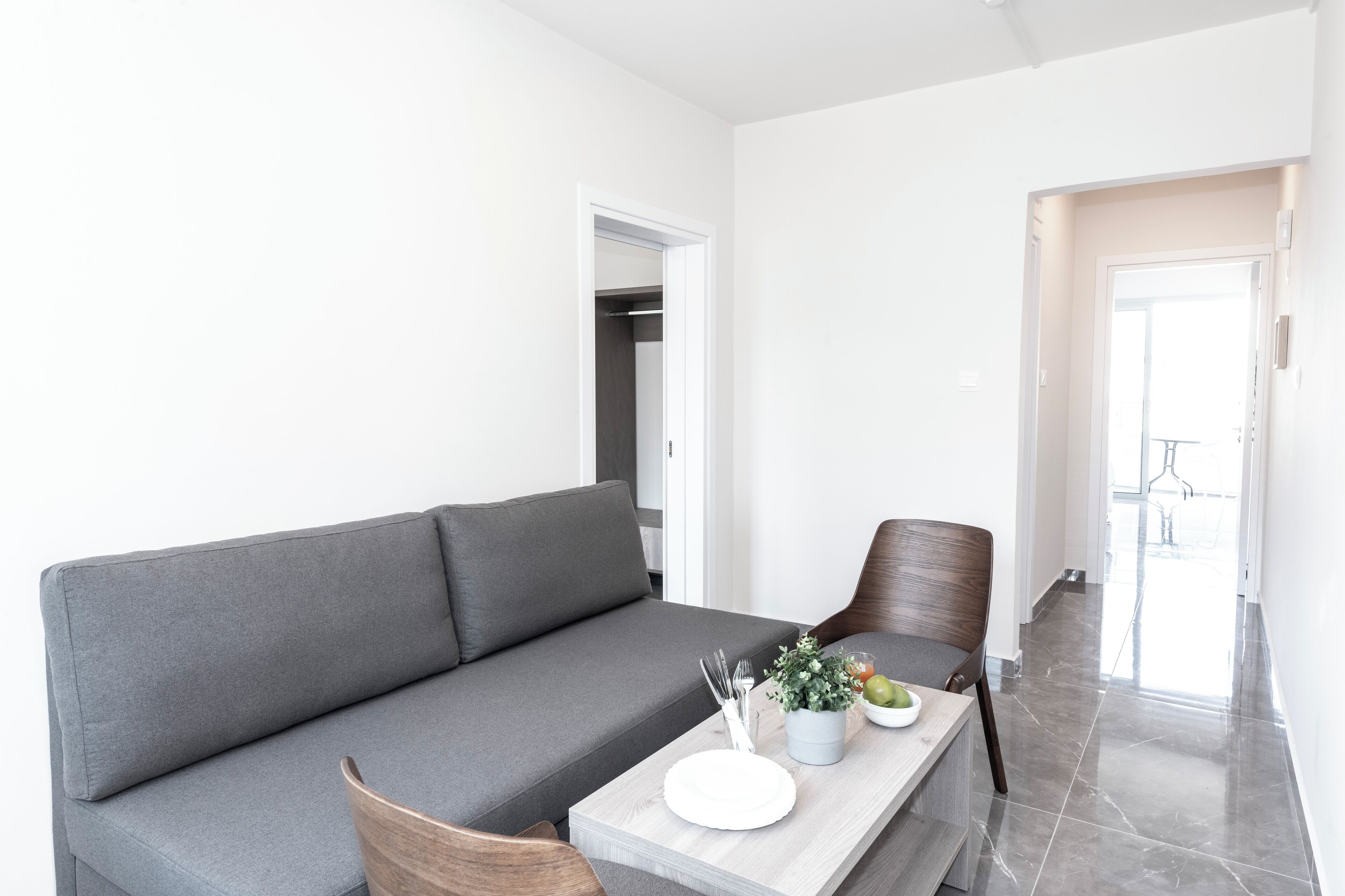 A modern living room with a grey sofa, a wooden coffee table, and a dining area with a white table set.