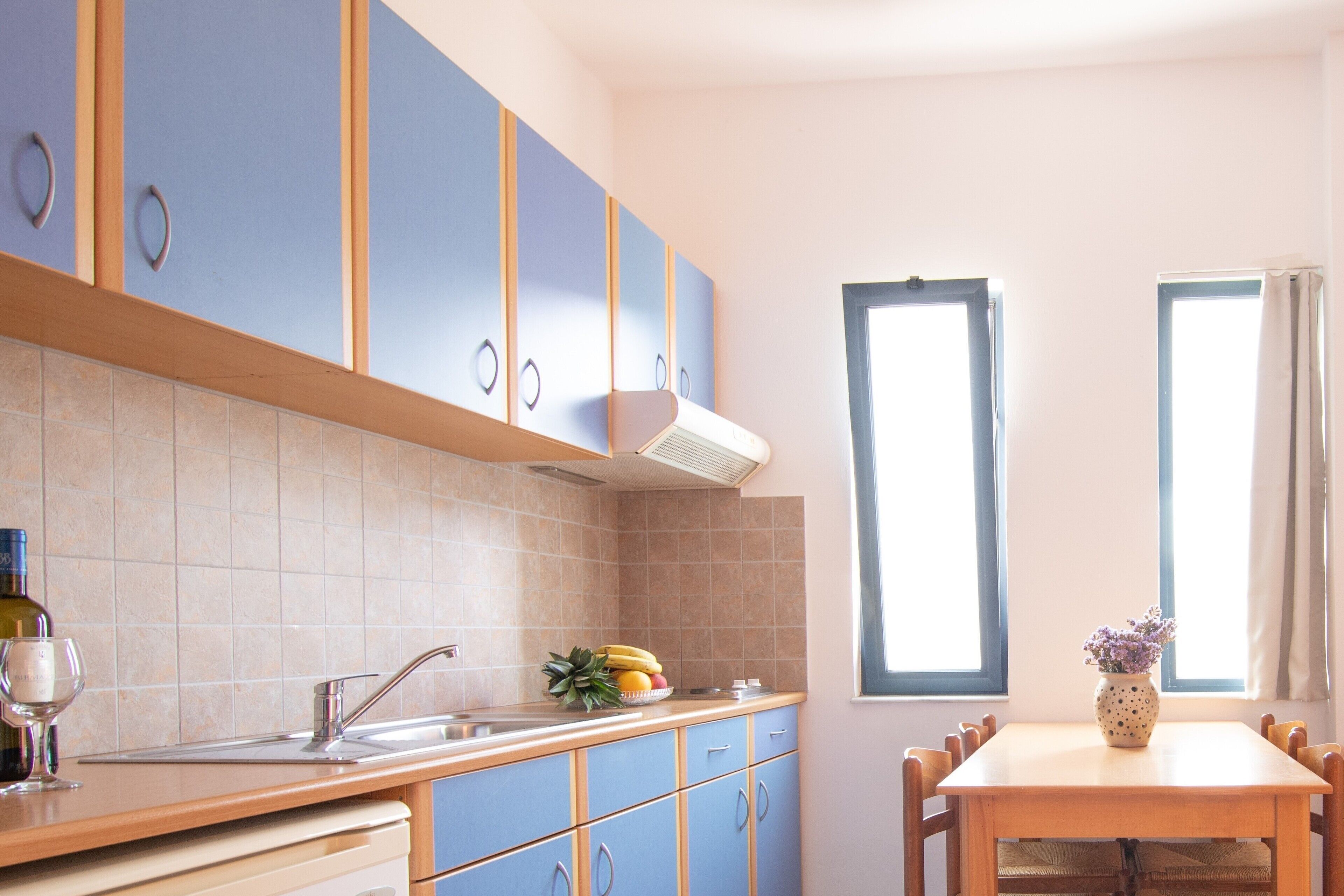 A kitchen with blue cabinets, a wooden countertop, a sink, and a dining table with chairs.