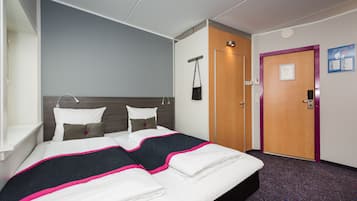 Et hotelværelse med en seng, et skab, en dør og en vægmonteret lampe.