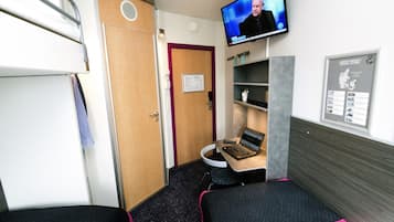 Une chambre d’hôtel compacte avec des lits superposés, un bureau avec un ordinateur portable, une télévision et une carte accrochée au mur.