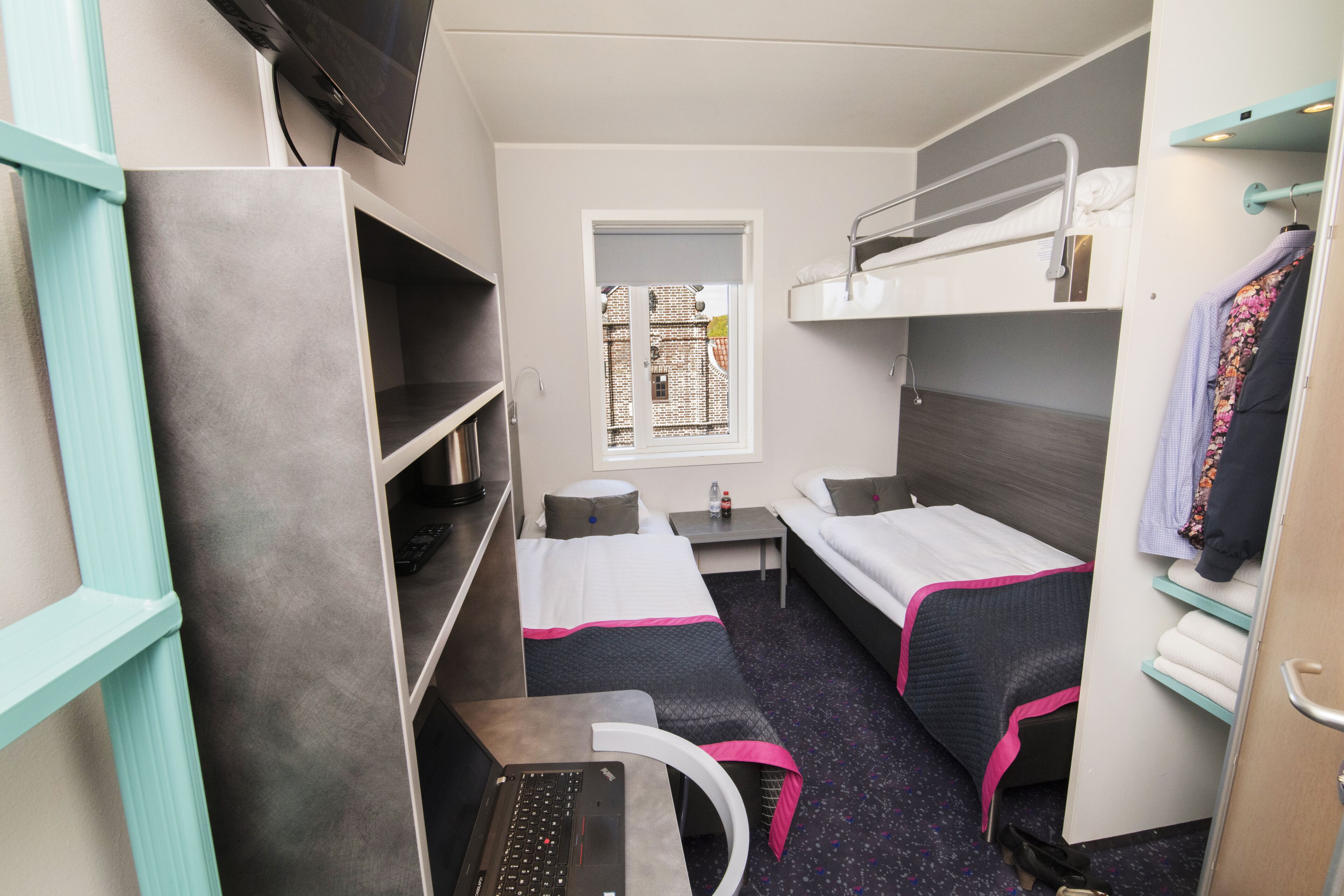 A compact hotel room with bunk beds, a desk, a chair, and a small window.