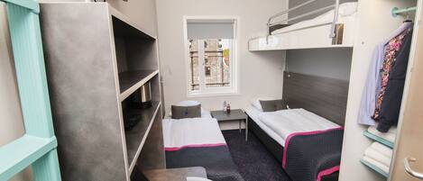 Habitación de hotel compacta con literas, un escritorio, una silla y una ventana pequeña.