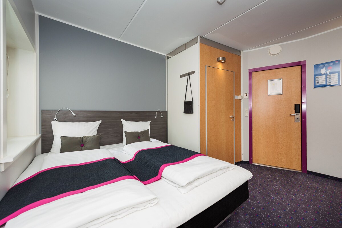 A hotel room with a bed, a wardrobe, a door, and a wall-mounted light fixture.