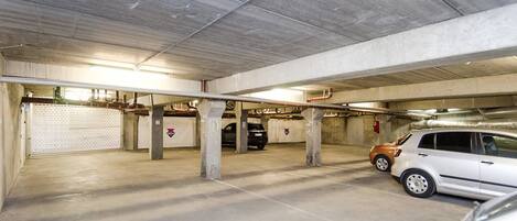 Un parking souterrain avec des piliers en béton, une voiture blanche et une voiture noire qui y sont garées.