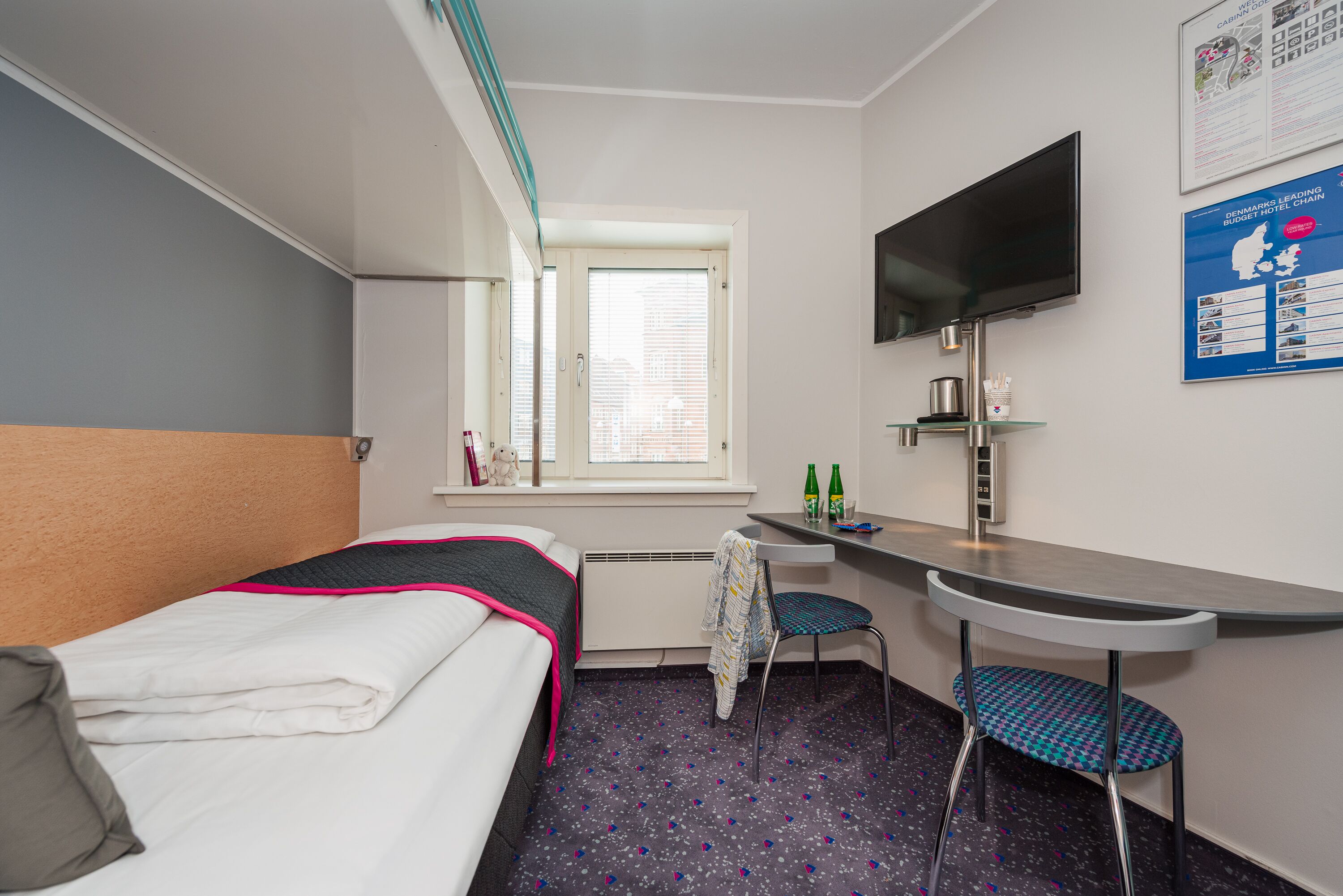A hotel room with a bed, a desk, a chair, a TV, and a window with blinds.