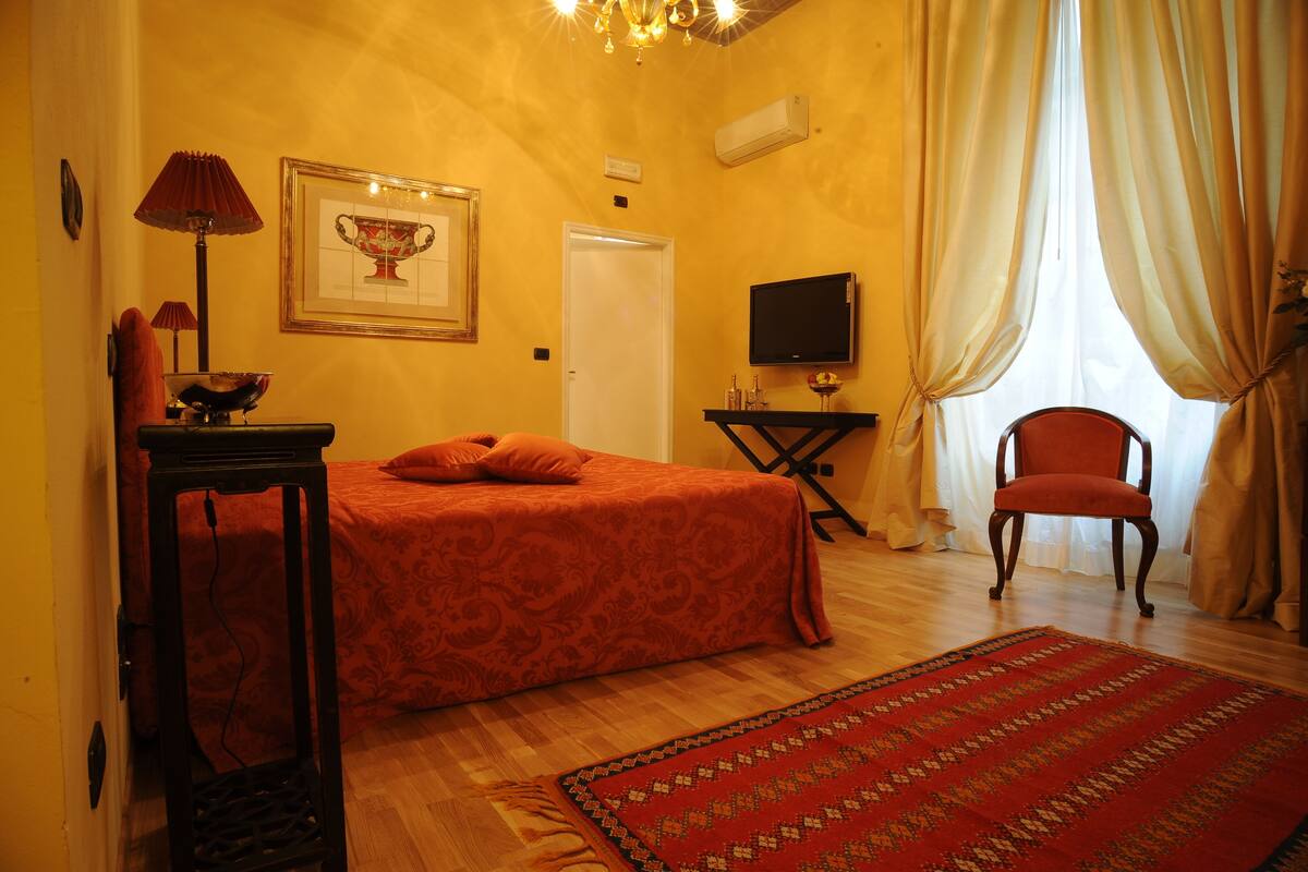 Una habitación de hotel con una cama, televisión, silla y alfombra.