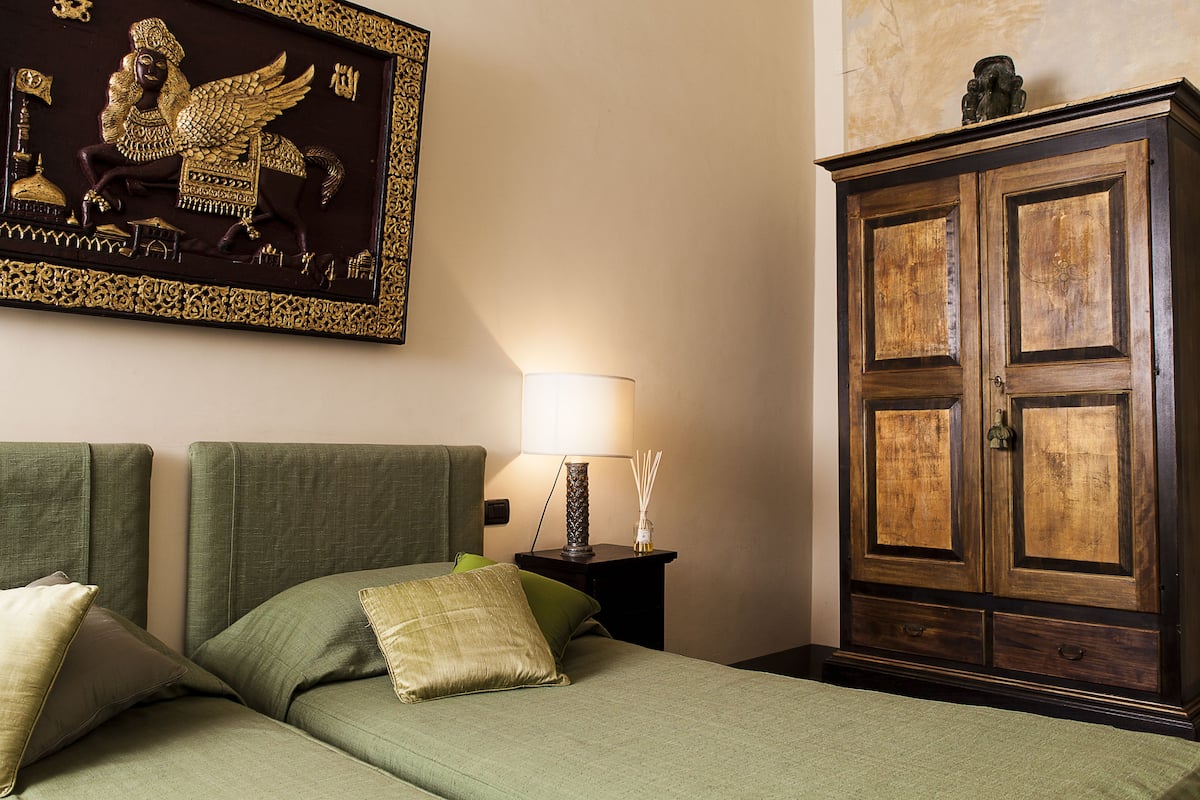 Un dormitorio con una cama verde, una mesita de noche con lámpara y un armario de madera.