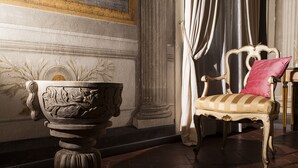 Une pièce comprenant un vase en pierre, un fauteuil avec un coussin et un rideau tombant en draperie.