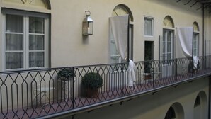 Un balcon doté d’une balustrade en fer forgé, de plantes en pot et d’un rideau blanc qui recouvre partiellement une fenêtre.