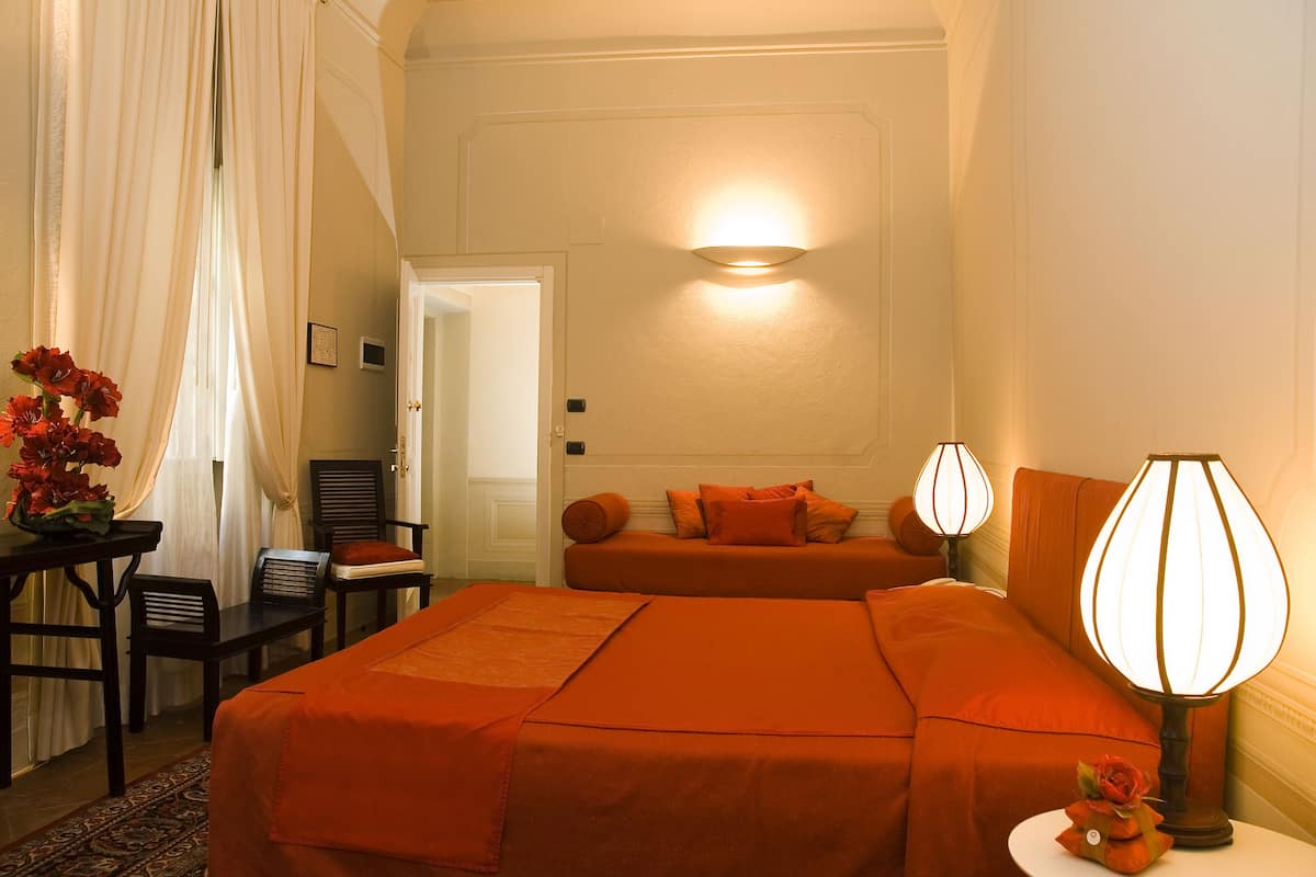 Una habitación de hotel con cama, escritorio, silla, lámpara y un jarrón con flores.