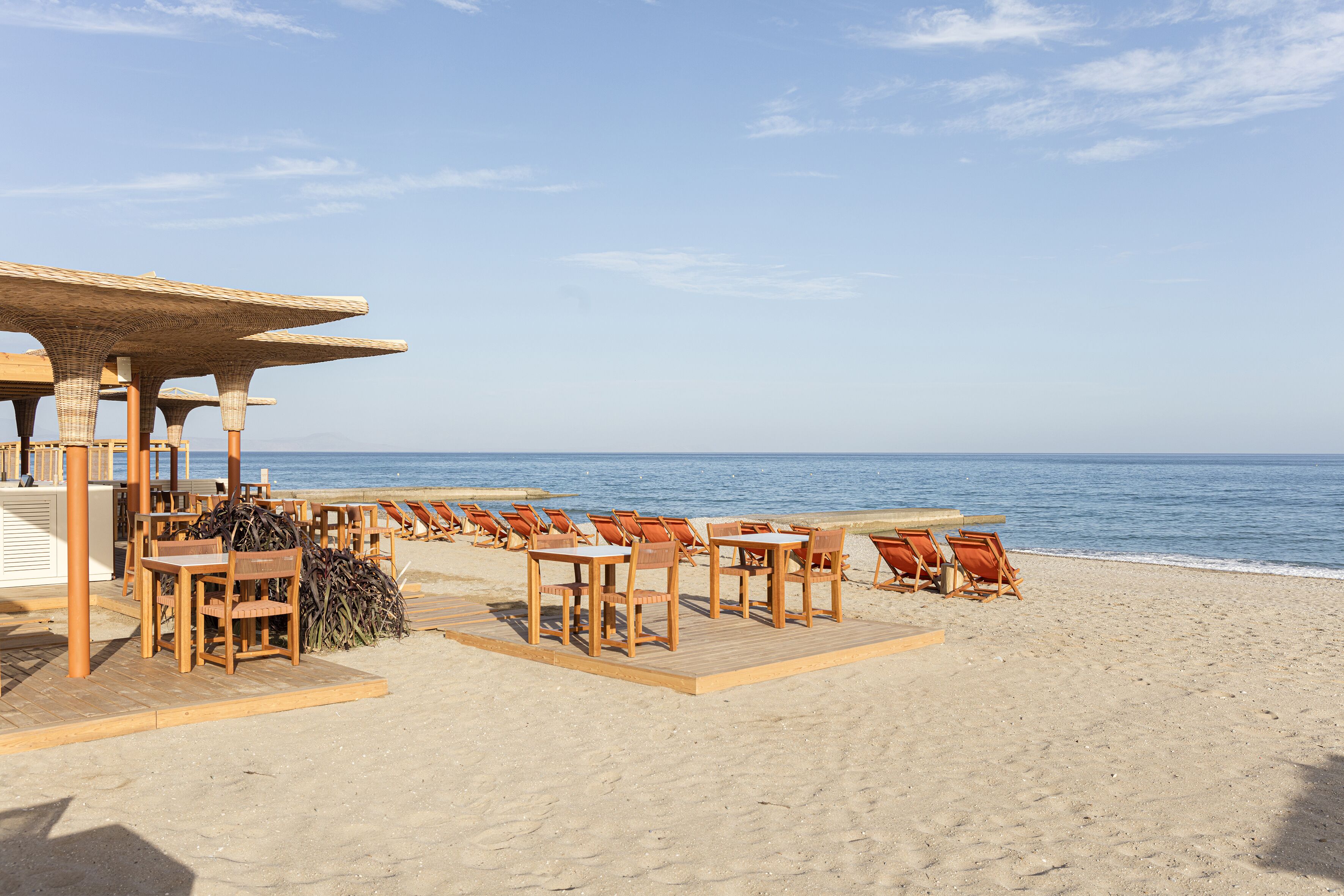 A beachside restaurant with outdoor seating, including tables and chairs, overlooking the ocean.