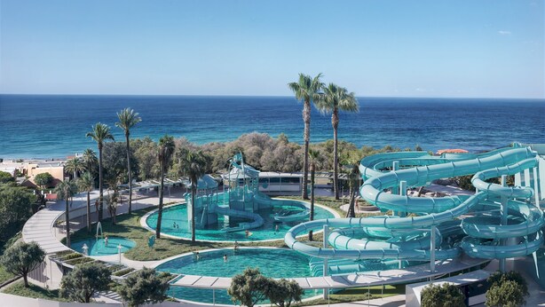 Parque acuático con varias toboganes y piscinas, rodeado de palmeras y con vistas al océano.