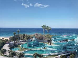 Parque acuático con varias toboganes y piscinas, rodeado de palmeras y con vistas al océano.