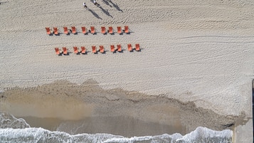 An aerial view of a beach with rows of orange beach chairs and a few people walking.