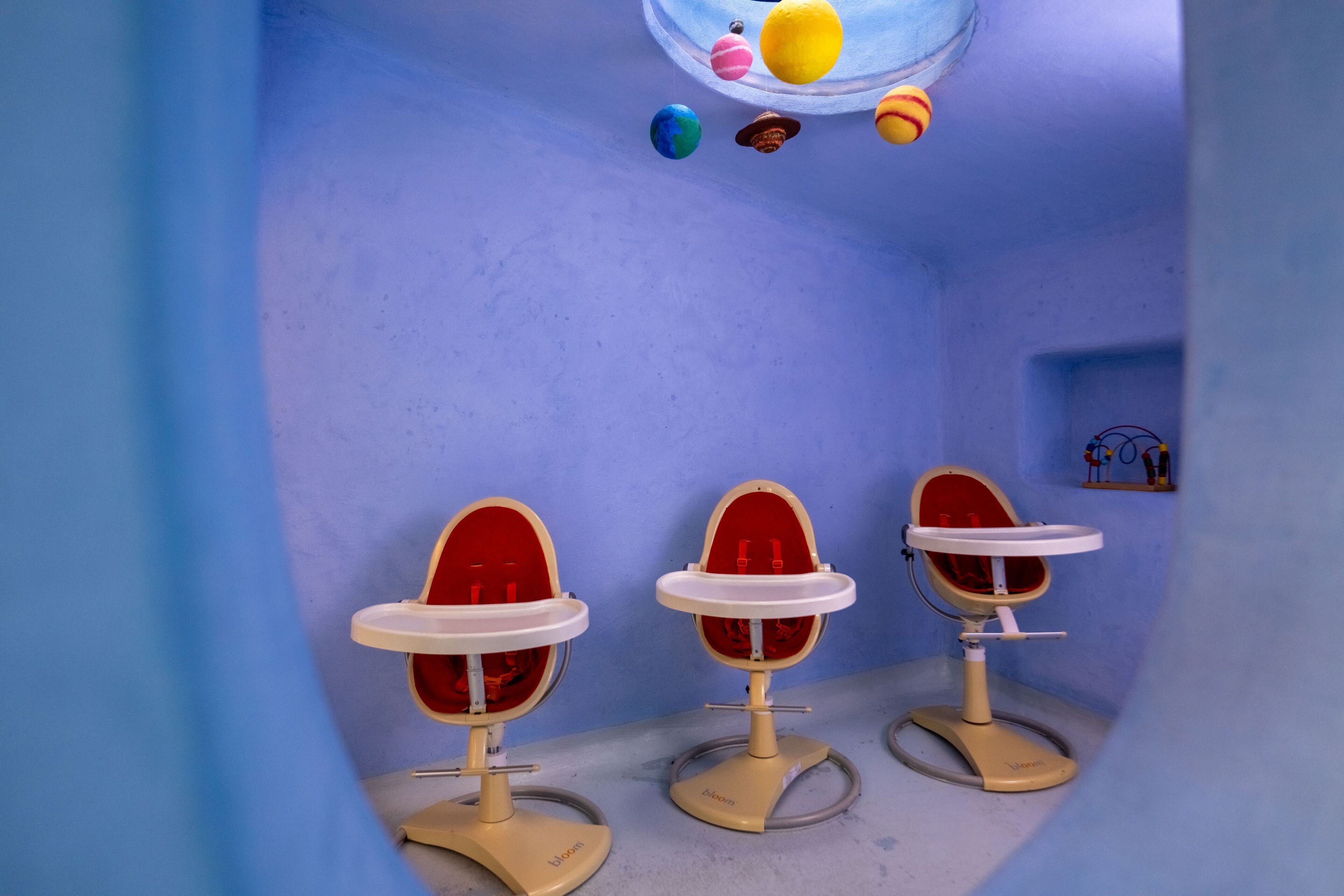 A room with three red and white high chairs against a blue wall, a small shelf with figurines, and a globe hanging from the ceiling.