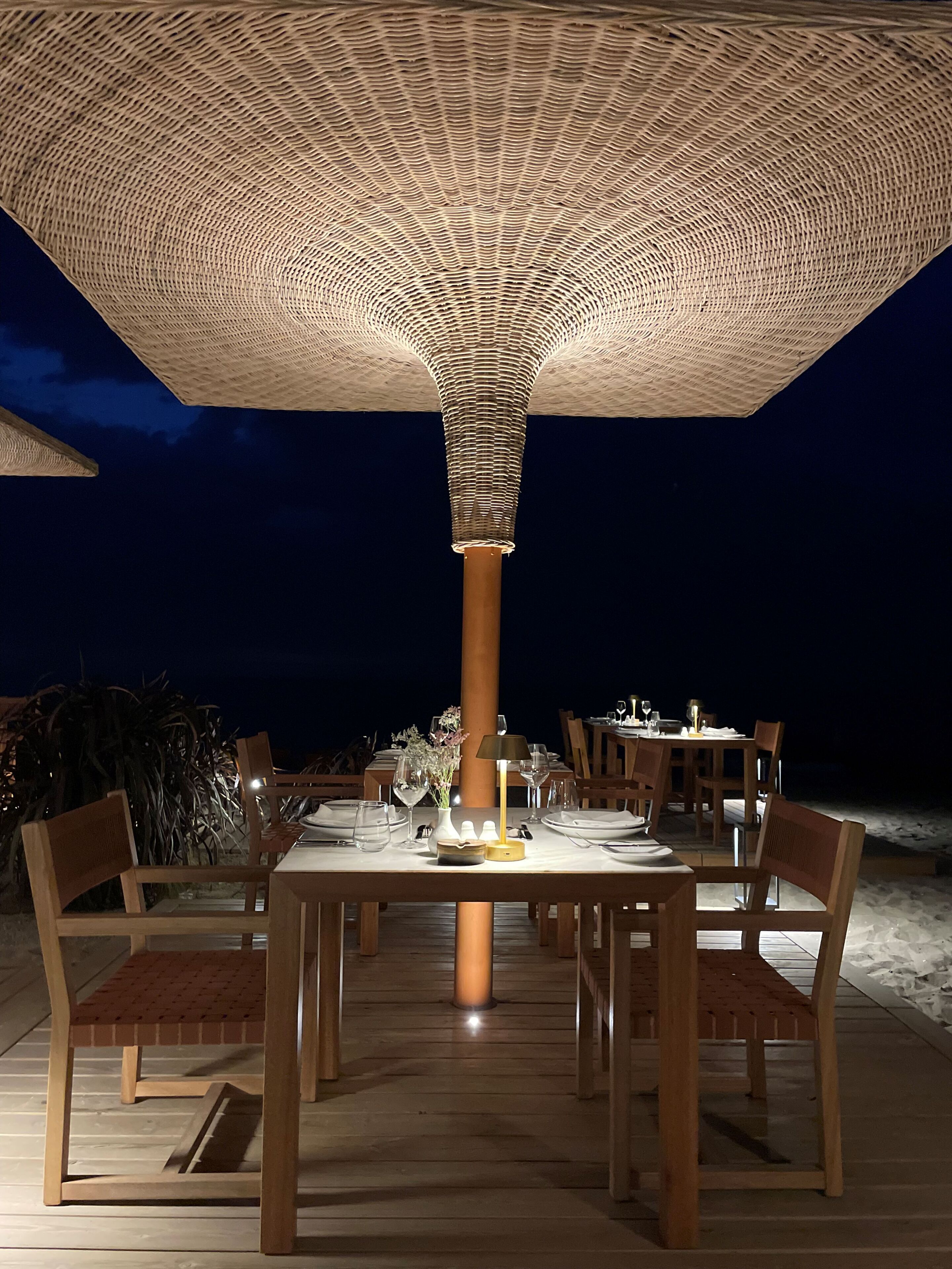 An outdoor dining area with a patterned canopy, wooden tables, and chairs.